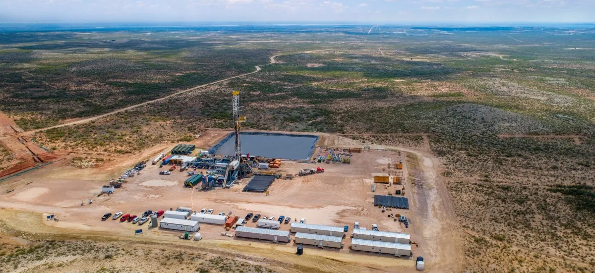 Vue aérienne d’un site de forage d’hydrocarbures isolé au milieu d’une plaine semi-aride, avec sa tour de forage, son bassin de rétention et ses bâtiments de chantier